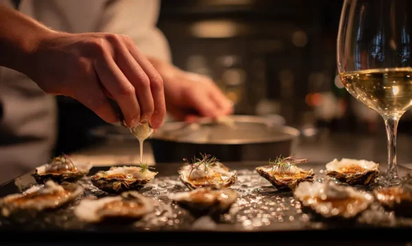 Cuisinier versant de la crème sur des huîtres avant cuisson, préparation gourmande